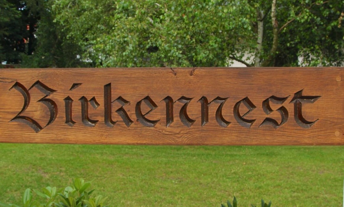 Holzschild mit der Aufschrift Birkennest vor Bäumen und Rasen